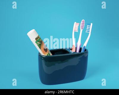 Un ensemble de trois brosses à dents multicolores, un tube de dentifrice écologique dans un récipient en céramique sur fond bleu Banque D'Images