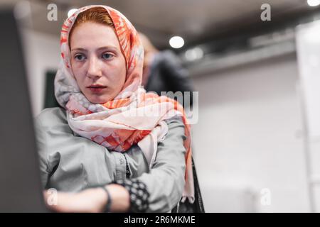 Jeune fille en fauteuil roulant portant un hijab travaillant sur son ordinateur portable au bureau Banque D'Images