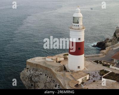 Un paysage côtier pittoresque avec un phare rouge et blanc vivant situé à côté d'un océan bleu tranquille avec plusieurs petits bateaux dans l'eau Banque D'Images