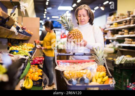 Femme âgée satisfaite cueillant de l'ananas mûr au supermarché Banque D'Images