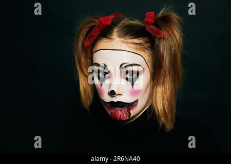 Gros plan portrait d'une jeune fille adolescente avec maquillage pour Halloween, coiffeur avec deux queues de porc et rubans rouges, fond noir Banque D'Images