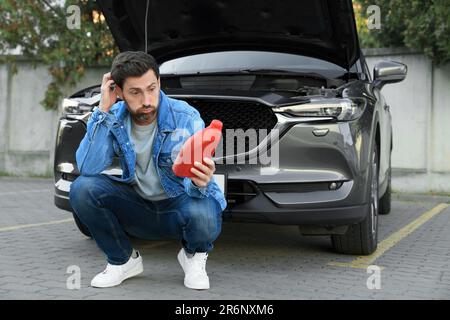 Homme perplexe tenant un contenant rouge d'huile à moteur près de la voiture à l'extérieur Banque D'Images