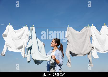 Femme accrochant des vêtements avec des épingles à linge sur la ligne de lavage pour sécher contre le ciel bleu Banque D'Images