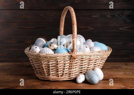 Panier en osier avec œufs de Pâques décorés avec soin sur une table en bois Banque D'Images