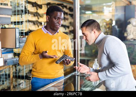 Vendeur consultant acheteur sur le pistolet dans la boutique d'armes Banque D'Images