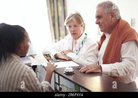 Réception, hôtel et couple senior en vacances ou personne âgée au concierge, à la réception ou à l'enregistrement auprès du réceptionniste ou du secrétaire du hall. Femme noire Banque D'Images