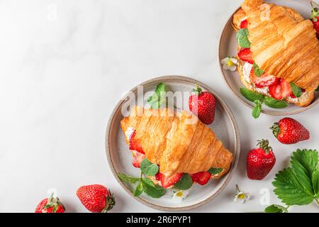 Sandwich croissant français avec fraises fraîches mûres et fromage à la crème dans une assiette avec fleurs sur fond blanc Banque D'Images
