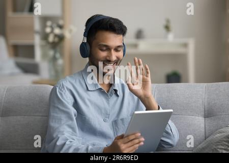 Jeune étudiant indien joyeux dans des écouteurs appréciant la conversation en ligne Banque D'Images