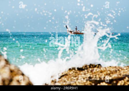 Koh Lanta, Thaïlande - 4 janvier 2014 : bateau de pêche traditionnel thaïlandais à longue queue avec des gens dans la mer derrière les éclaboussures d'eau Banque D'Images