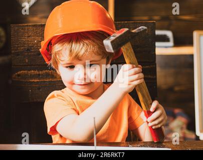 Un petit garçon avec un marteau fait des réparations. L'enfant participe activement au processus fait à la main. Banque D'Images