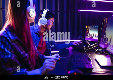 Deux jeunes joueurs, un homme et une femme, participent à un concours de jeu sur une plate-forme virtuelle. Assis devant une configuration à plusieurs moniteurs, Young Gen Z g Banque D'Images
