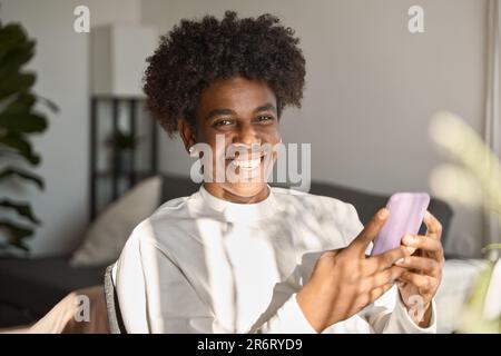 Heureux gen z Africain américain adolescent utilisant le téléphone portable à la maison, portrait. Banque D'Images