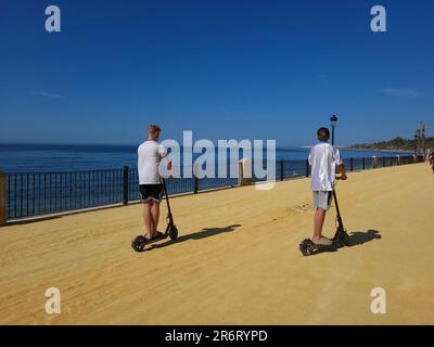 Deux jeunes garçons qui font du scooter électrique sur la promenade de Marbella, en Espagne. Banque D'Images