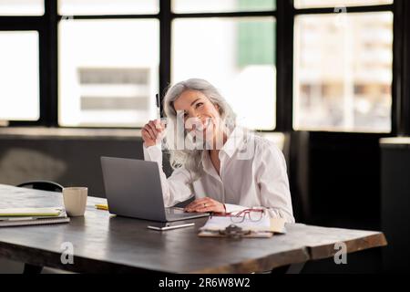 Femme d'affaires souriante assise sur un ordinateur portable travaillant à l'intérieur du bureau Banque D'Images