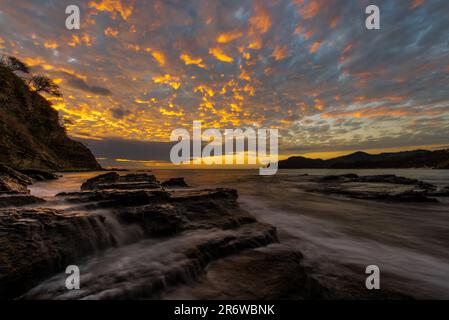 Photo de paysage de longue exposition de l'eau de l'océan pacifique qui coule sur les rochers de la plage avec un coucher de soleil coloré près de San Juan del sur au Nicaragua Banque D'Images