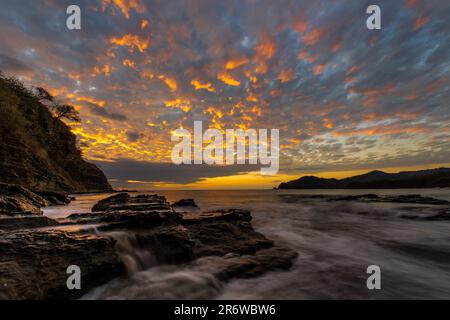 Photo de paysage de longue exposition de l'eau de l'océan pacifique qui coule sur les rochers de la plage avec un coucher de soleil coloré près de San Juan del sur au Nicaragua Banque D'Images