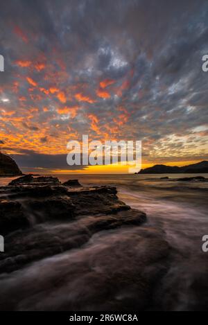 Photo de paysage de longue exposition de l'eau de l'océan pacifique qui coule sur les rochers de la plage avec un coucher de soleil coloré près de San Juan del sur au Nicaragua Banque D'Images