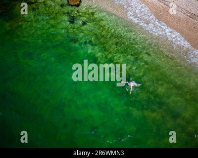 Femme se baignant et nageant sur la côte du Péloponnèse en eau verte et cristalline sur une plage romantique avec des rochers et une forêt en arrière-plan Banque D'Images