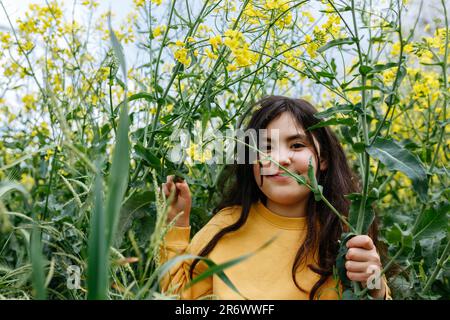 fille souriante avec de longs cheveux dans les stands jaunes haut dans le champ avec des fleurs jaunes Banque D'Images