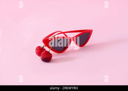 Lunettes de soleil rouges en forme de chat avec deux cerises sur fond rose pastel. Concept d'été surréaliste du printemps minimal pour la publicité, le papier peint Banque D'Images