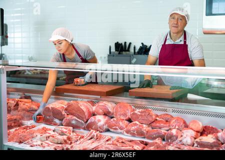 Propriétaire d'une boucherie âgée debout derrière une vitrine avec de la viande Banque D'Images