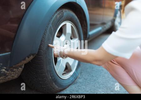 Accident de voiture. Gros plan sur une femme voyageur en ville touchant un pneu crevé. Banque D'Images