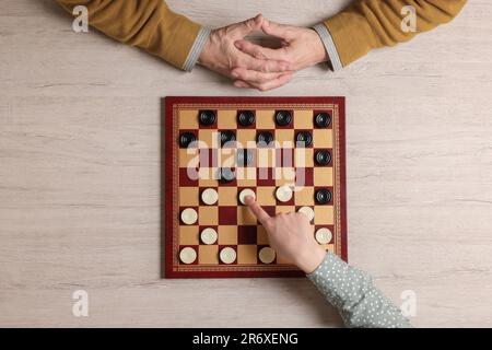 Homme senior jouant aux dames avec une femme à une table en bois blanc, vue de dessus Banque D'Images