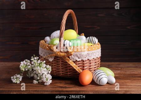 Panier en osier avec des œufs de Pâques décorés avec soin et des fleurs de lilas blanc sur une table en bois Banque D'Images