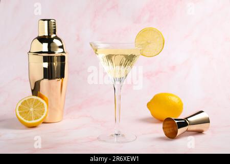 Un verre de Martini de cocktail rafraîchissant avec une tranche de citron et des fruits frais près d'un shaker sur fond de marbre rose Banque D'Images