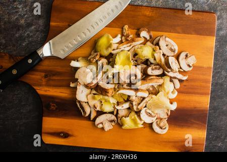 Champignons sauvages tranchés avec un couteau de chef sur une planche à découper en bois : huîtres préparées, shiitake et champignons crimini empilés sur une planche à découper Banque D'Images