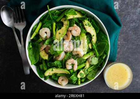 Salade d'épinards nappée de crevettes, d'asperges et d'avocat : salade saine dans un bol de service avec vinaigrette au citron sur le côté Banque D'Images