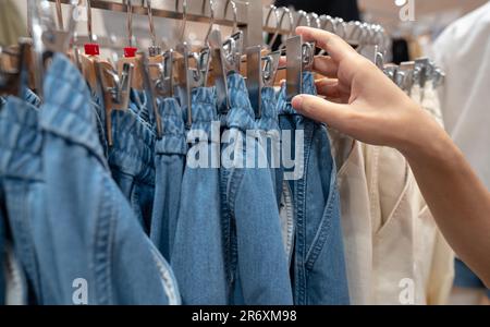 Femme magasiner des pantalons en denim dans un magasin de vêtements. Femme choisissant des vêtements. Jean sur le cintre suspendu sur le porte-vêtements dans le magasin de vêtements. Boutique de mode à l'intérieur Banque D'Images