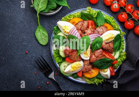 Salade Périgord avec foie de poulet rôti, tomates rouges, concombres, œufs durs, laitue et épinards. Arrière-plan de la table de cuisine noire, vue du dessus Banque D'Images