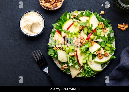 Salade Waldorf aux pommes rouges et vertes, céleri cru, laitue, arugula et noix avec sauce mayonnaise, fond de table noir, vue du dessus Banque D'Images