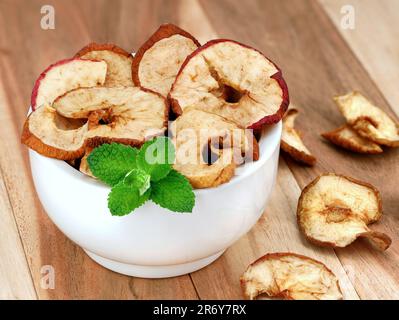 Croustilles de pomme séchées faites maison garnies de feuilles de menthe dans un bol blanc sur fond de bois, délicieux en-cas de pomme végétalienne sans additifs Banque D'Images