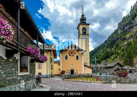 Église avec grande horloge sur le clocher et maisons décorées de fleurs dans la petite ville alpine de Gressoney la Trinite en Italie. Banque D'Images