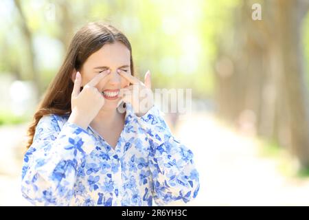 Femme stressée se grattant les yeux debout dans un parc ensoleillé Banque D'Images