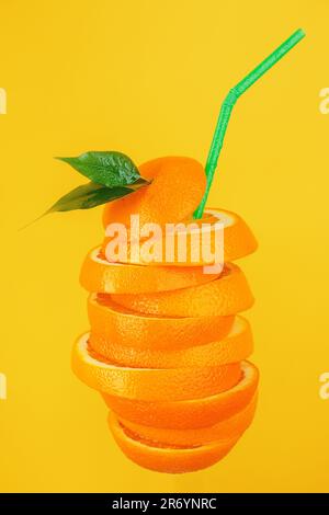 Des tranches d'orange juteuses sont coupées sous la forme d'un cocktail avec une paille sur fond jaune. Boisson rafraîchissante au jus d'orange. Idée de conception pour la publicité d'une boisson aux fruits. Banque D'Images