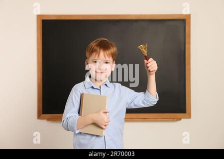 Petit garçon mignon sonnant la cloche de l'école dans la salle de classe Banque D'Images