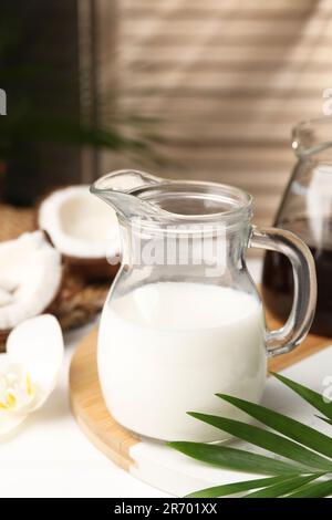 Pichet en verre de délicieux lait de coco sur table blanche à l'intérieur Banque D'Images
