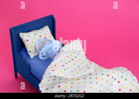Concept de congé de maternité. Lit en peluche avec sucette pour bébé sur fond rose Banque D'Images