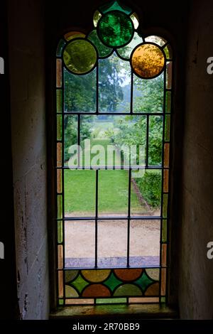 Painswick Rococo Gardens, Painswick, Gloucestershire - une vue sur les jardins à travers une fenêtre en vitrail de la Maison Rouge dans les jardins Banque D'Images