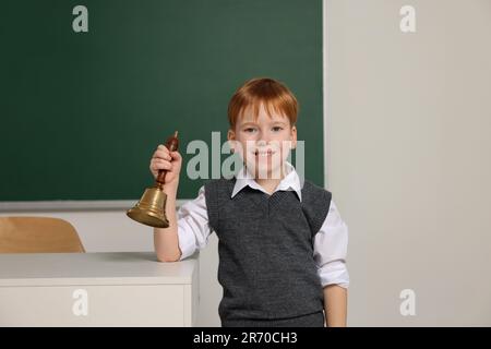 Petit garçon mignon sonnant la cloche de l'école dans la salle de classe Banque D'Images