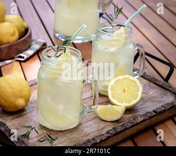 Limonade en deux verre jaes avec des tranches de citron, du romarin et de la glace sur un plateau en bois Banque D'Images