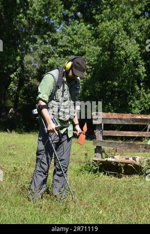 Ville:Marilia, Sao Paulo, Brésil, 25 mars 2023: Homme portant une casquette utilisant un détecteur de métal dans un championnat de detectorisme sur un terrain herbeux avec des arbres i Banque D'Images