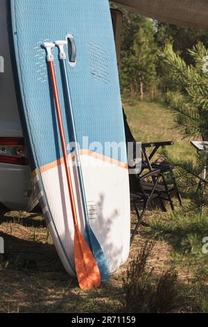 Les planches d'aviron gonflables Sup se tiennent près du camping-car gonflé dans la nature pendant la journée. Banque D'Images