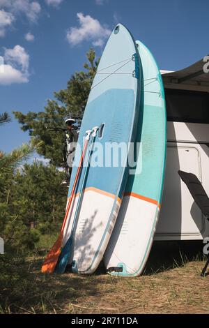 Les planches d'aviron gonflables Sup se tiennent près du camping-car gonflé dans la nature pendant la journée. Banque D'Images