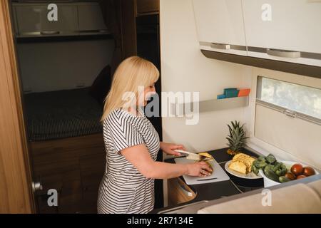 une femme cuisant de la nourriture dans la cuisine à l'intérieur d'un autocaravane, à l'intérieur d'un autocaravane. Banque D'Images