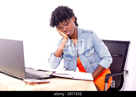 jeune fille étudiante fatiguée assise sur la table face à l'ordinateur et tenant la main sur la joue. Banque D'Images