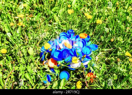 Pile de bouchons de bouteille en plastique coloré sur un pré vert avec des pissenlits en croissance. Photo de concept de la protection de l'environnement, littering de l'environnement Banque D'Images